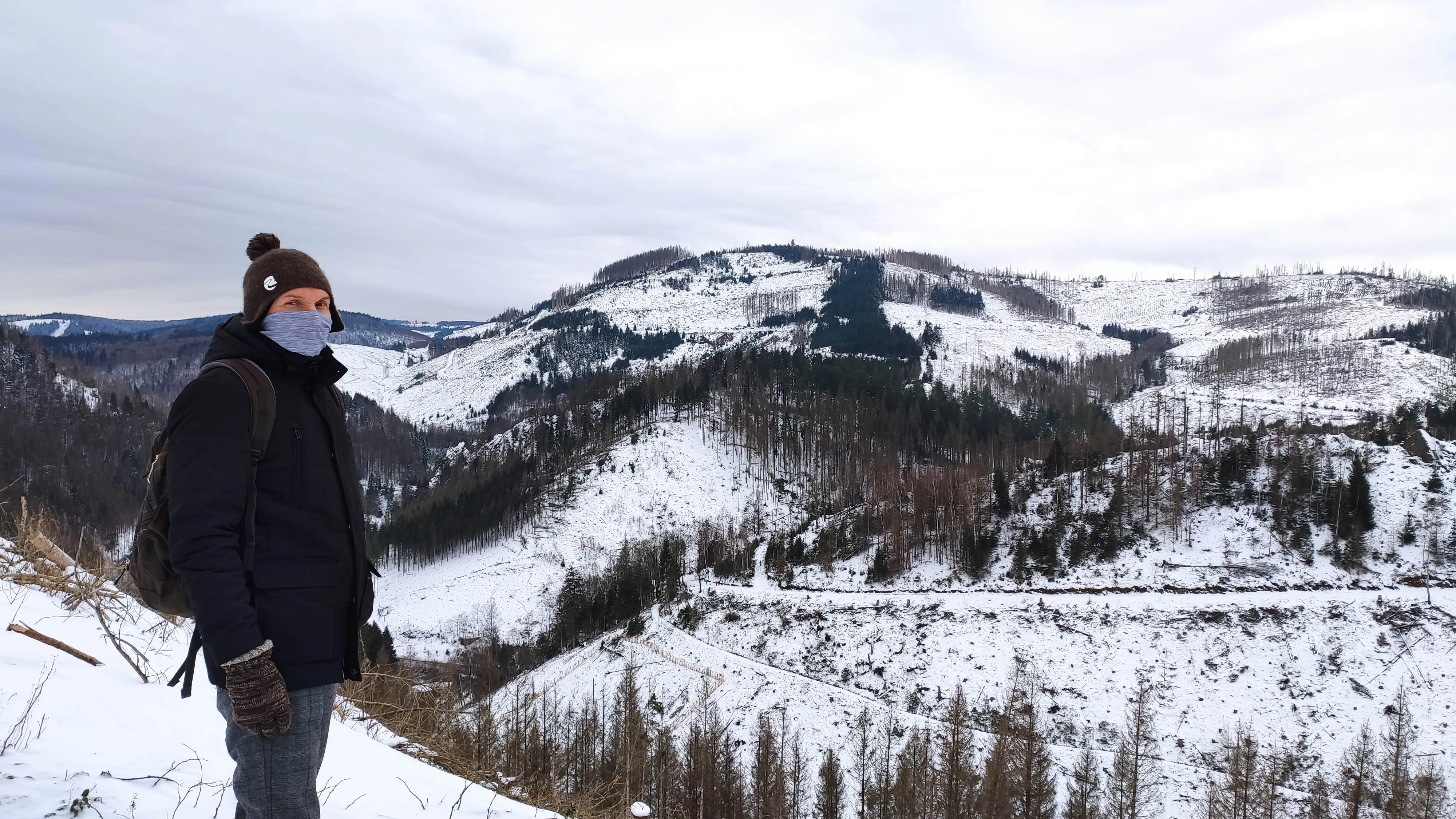 Stephan Blumenthal draußen bei Schnee auf einem Berggipfel mit Aussicht auf die Winterlandschaft